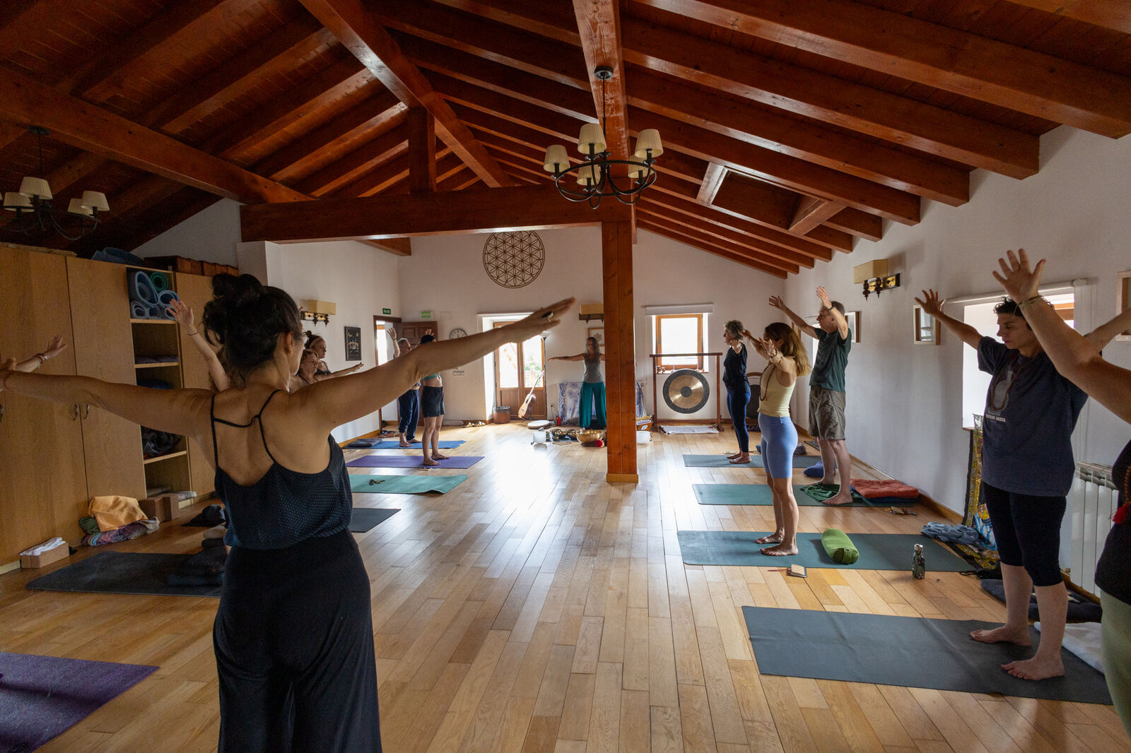 Grupo en postura de la montaña con los brazos en alto durante una clase de yoga, gong al fondo