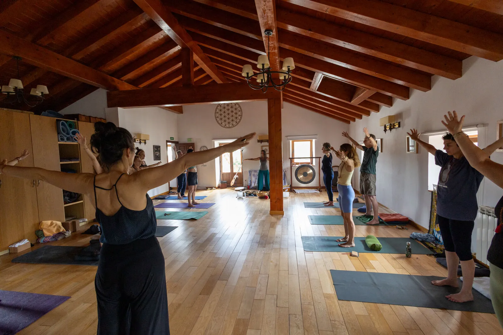 Grupo en postura de la montaña con los brazos en alto durante una clase de yoga, gong al fondo